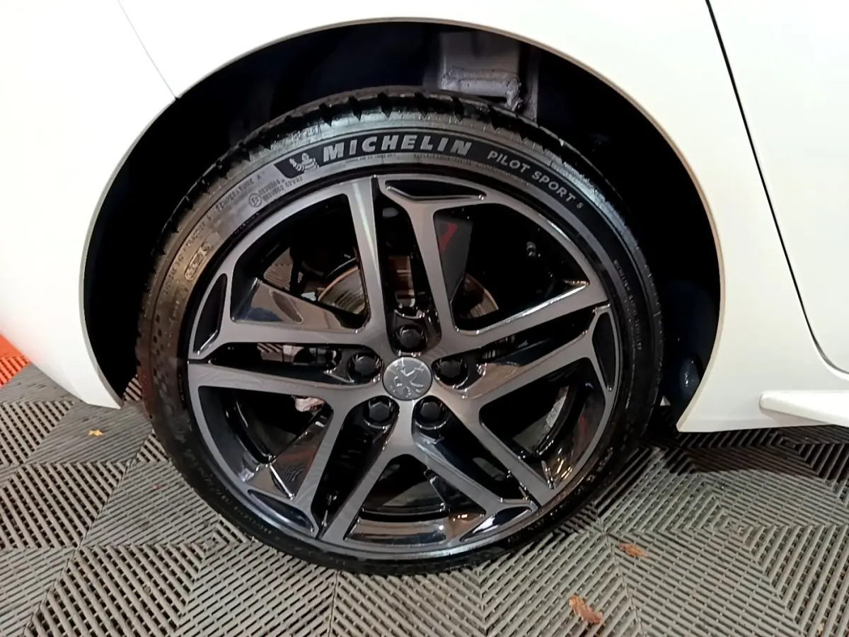 Gros plan sur la roue arrière droite noire brillante de la Peugeot 308 blanche, mettant en valeur la jante sport et le pneu Michelin.