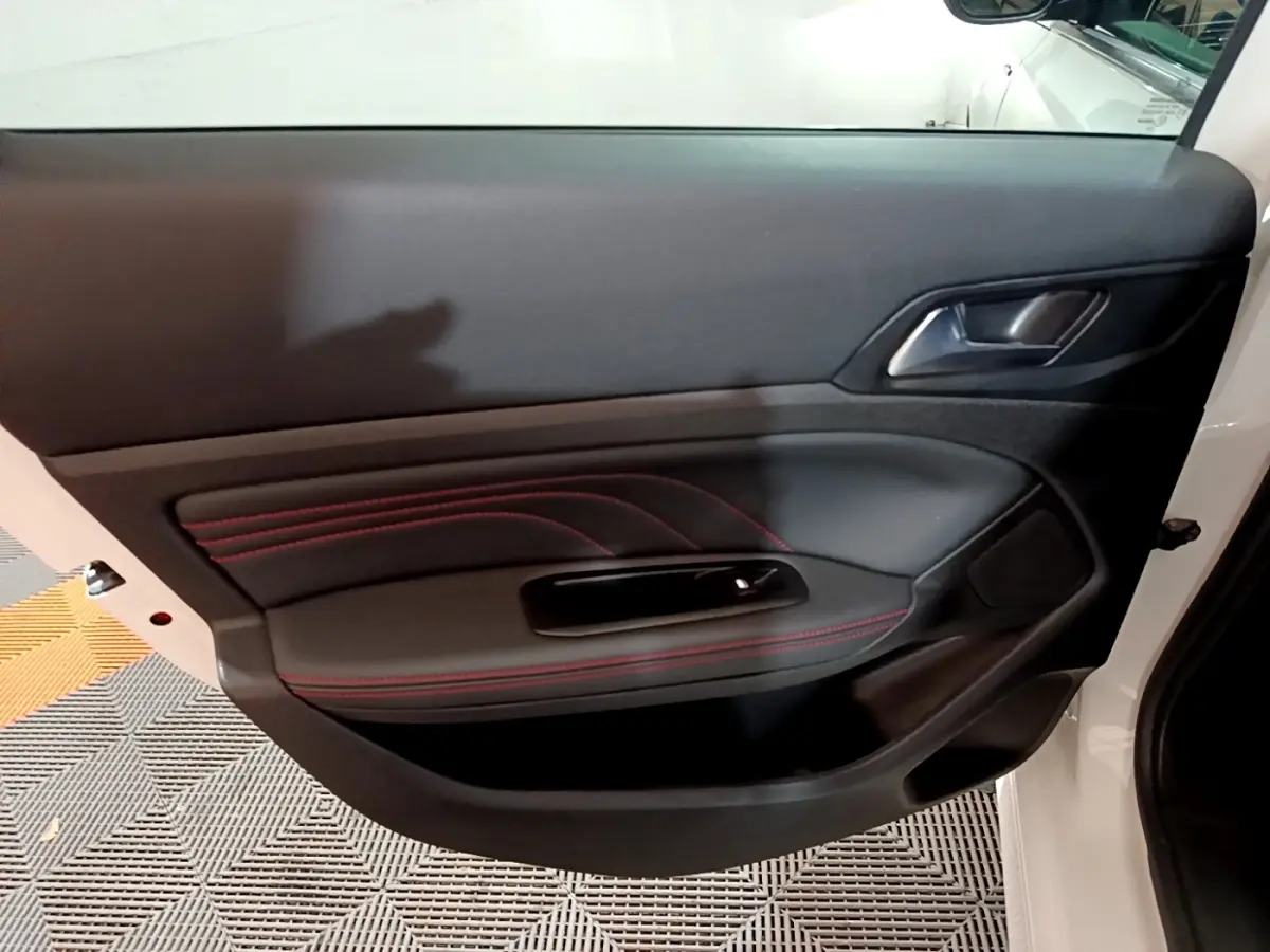 Gros plan sur la porte côté gauche d'une Peugeot 308 blanche, avec surpiqûres rouges et poignée intégrée.
