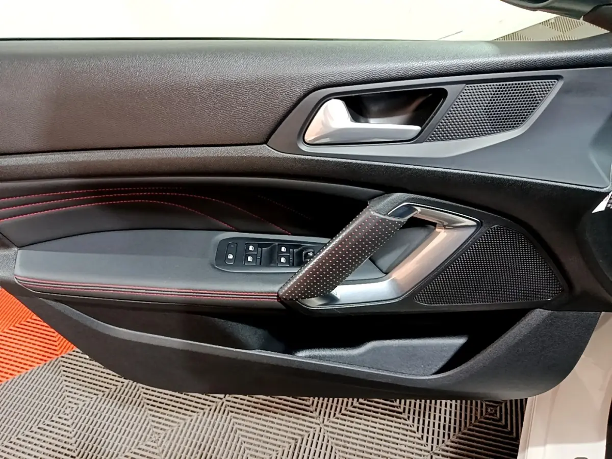 Vue rapprochée de la porte côté conducteur de la Peugeot 308 GT Line blanche, avec surpiqûres rouges et commandes électriques.