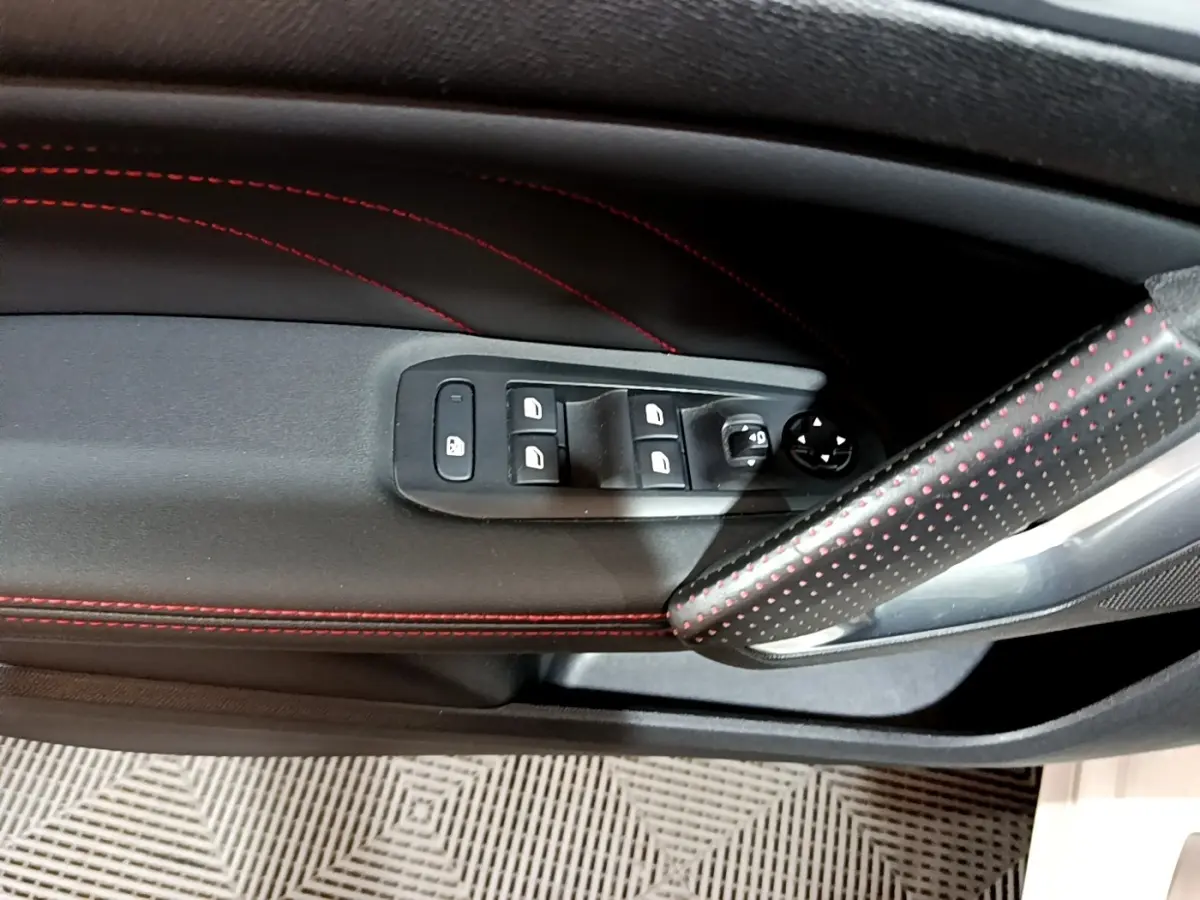Gros plan sur la porte côté gauche de la Peugeot 308 GT Line blanche, avec surpiqûres rouges et commandes des vitres.
