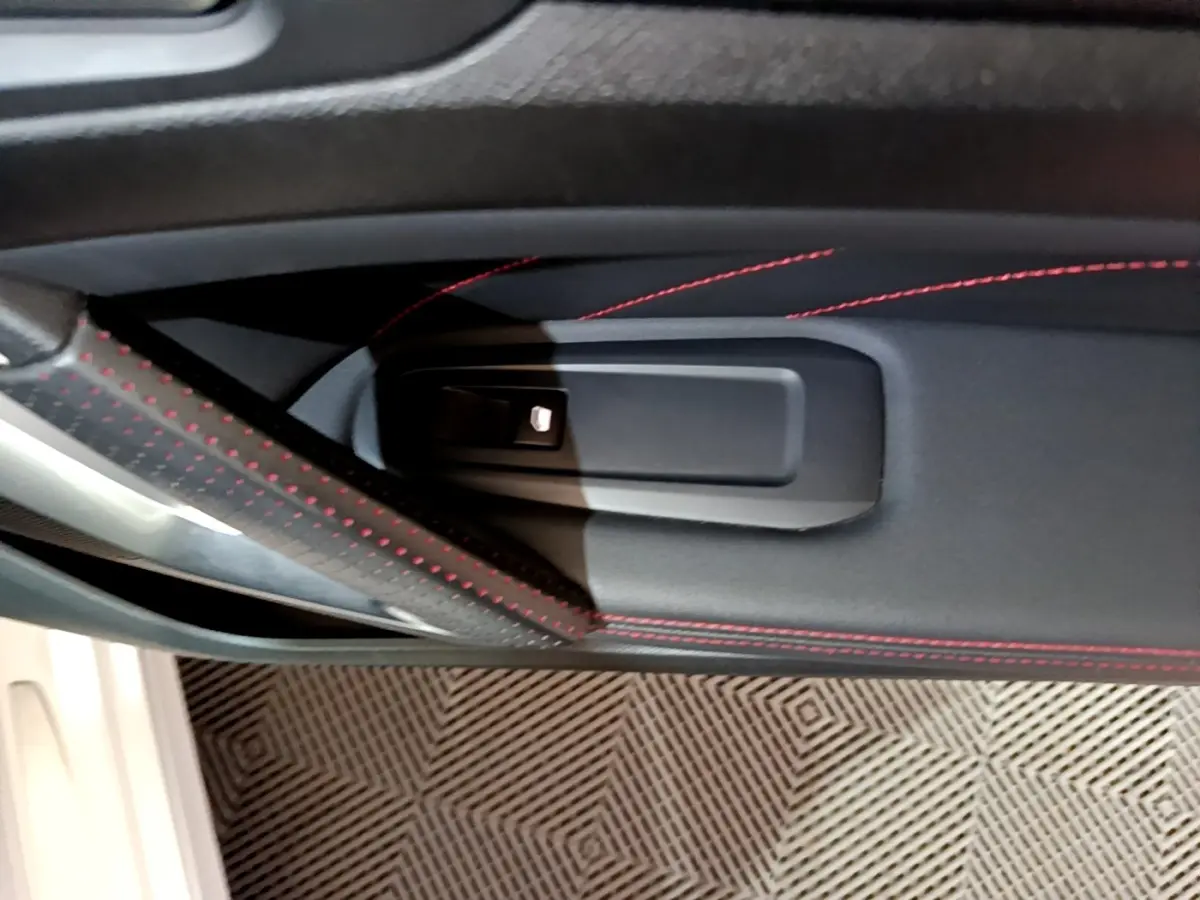Détail de la poignée intérieure côté gauche avec surpiqûres rouges sur la porte noire de la Peugeot 308 GT Line blanche.