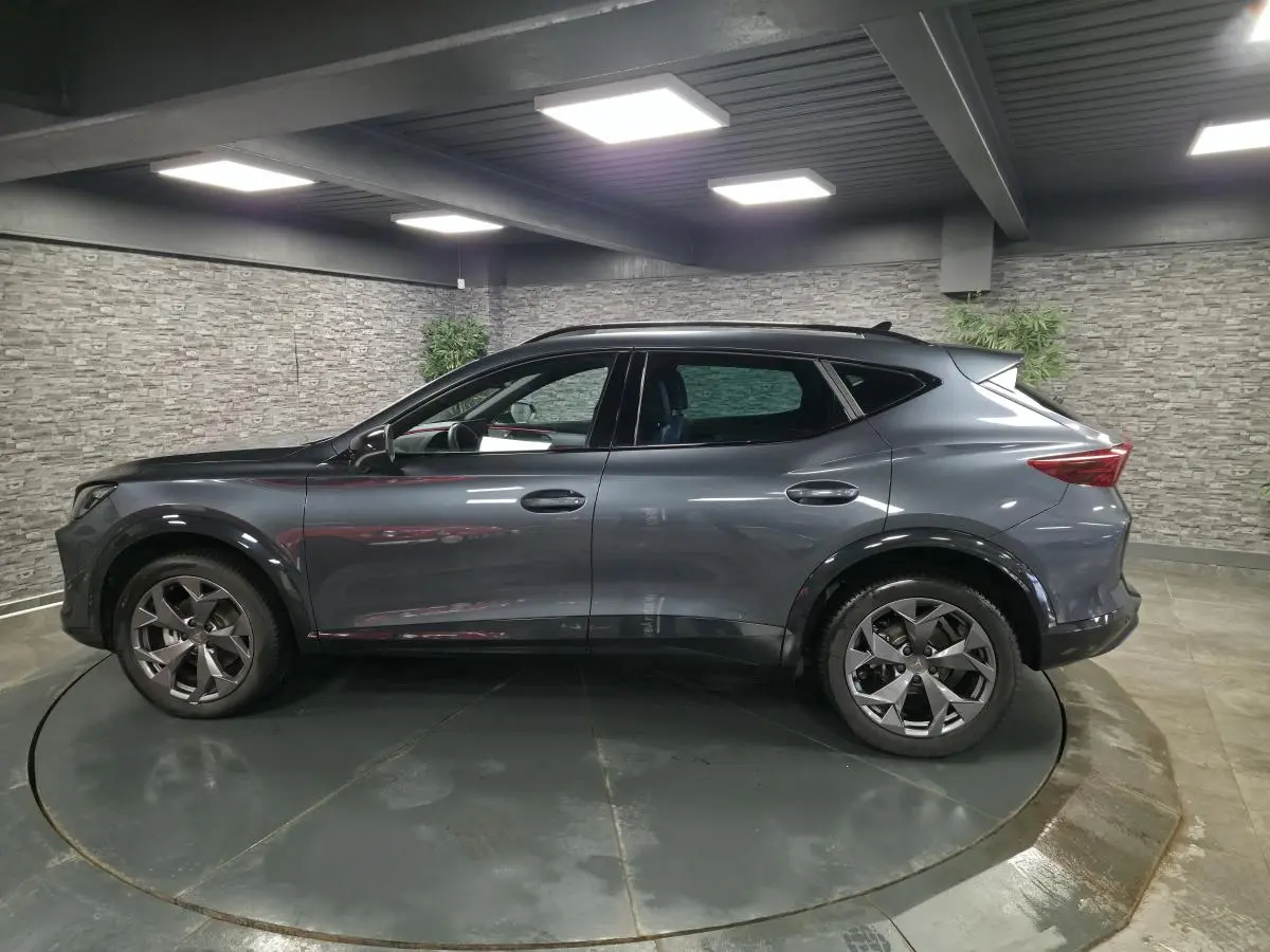 Vue de profil côté gauche d'un CUPRA Formentor gris métallisé 2025 avec jantes alliage 18'' et toit noir dans un garage.