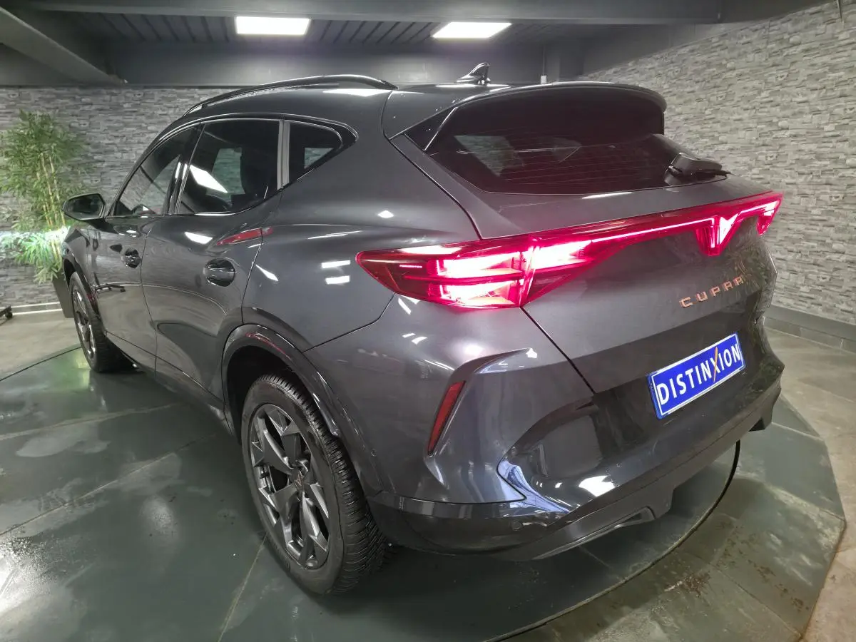 Vue 3/4 arrière droite du CUPRA Formentor gris métallisé avec feux arrière Tri-LED allumés et jantes alliage 18 pouces.