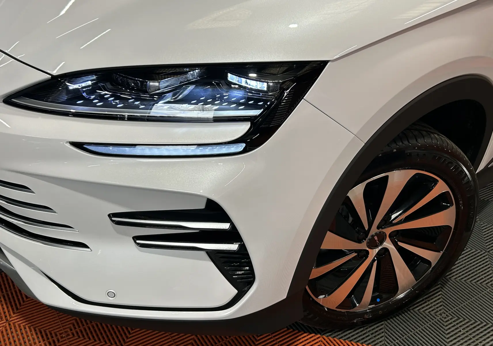 Gros plan sur l’avant droit blanc nacré du BYD SEAL U 2025, mettant en valeur le phare LED et la jante bicolore.