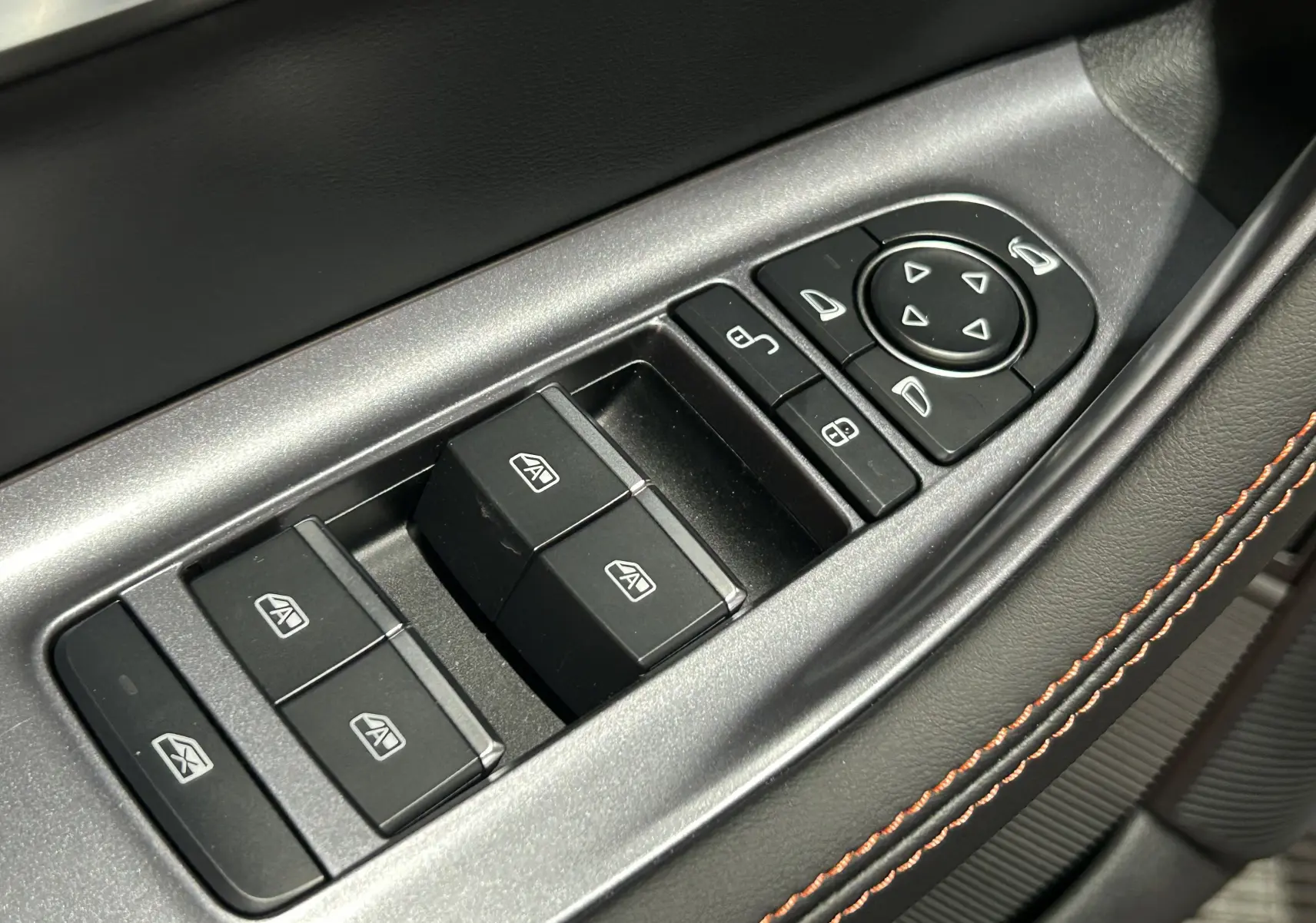 Gros plan sur les commandes de lève-vitres et réglages des rétroviseurs côté conducteur, avec surpiqûres orange sur cuir noir.