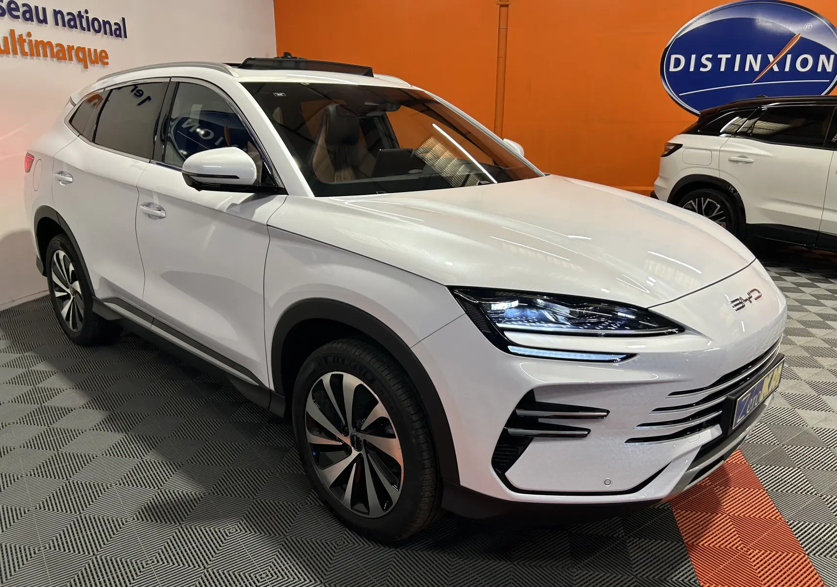 Vue 3/4 avant droite du SUV BYD SEAL U blanc nacré avec toit ouvrant et jantes bi-ton dans un showroom.