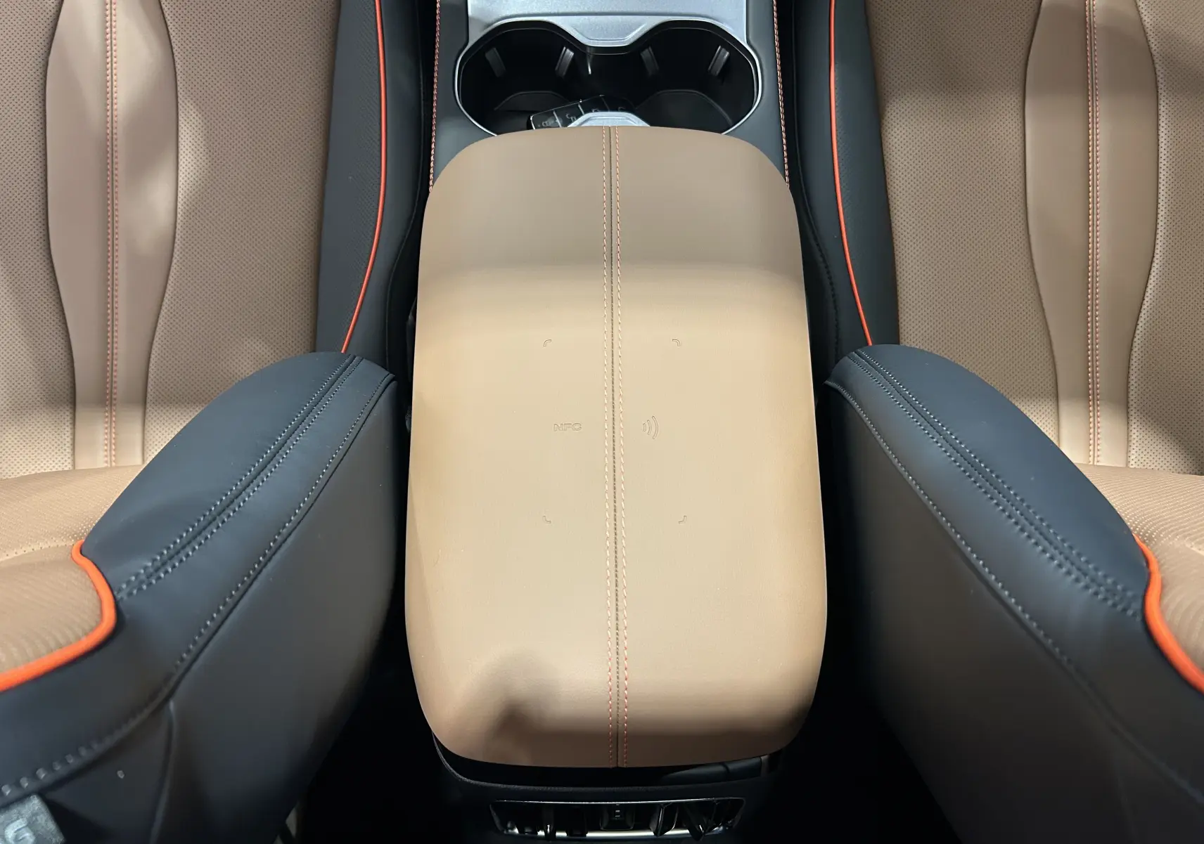 Vue rapprochée de l'accoudoir central en cuir marron avec surpiqûres orange, entre les sièges avant perforés du BYD SEAL U.
