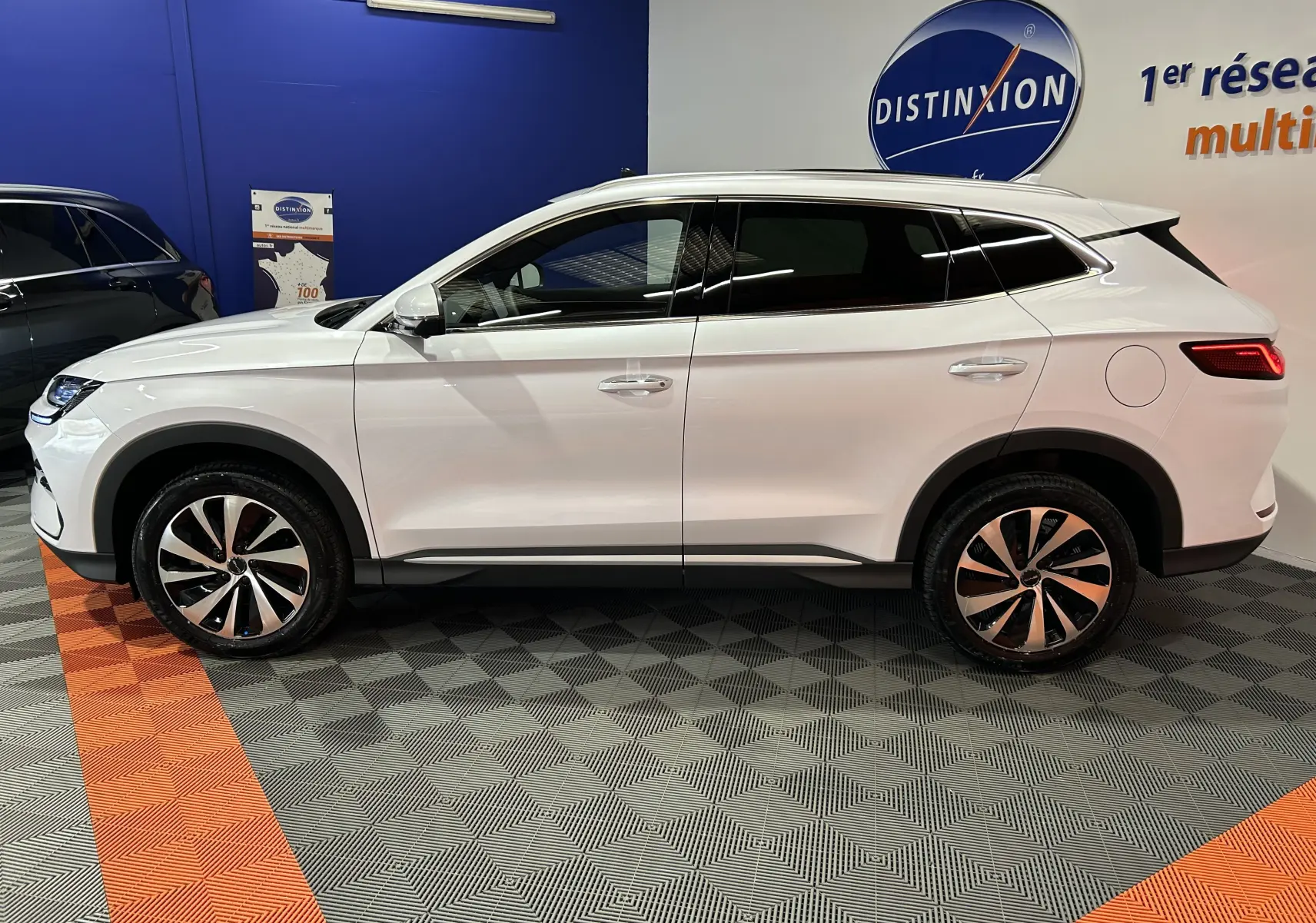 Vue de profil côté gauche d’un SUV BYD SEAL U blanc neige, avec jantes bicolores et vitres teintées, en intérieur showroom.
