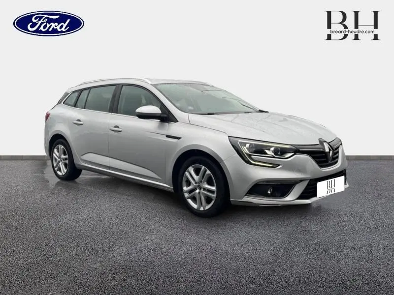 Renault Mégane Break gris platine vue 3/4 avant droit, avec feux LED et barres de toit visibles.