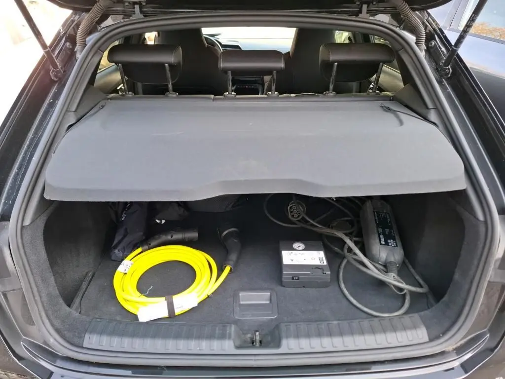 Coffre ouvert d’une Audi A3 Sportback noire, vue arrière, avec câble de recharge jaune et accessoires visibles.