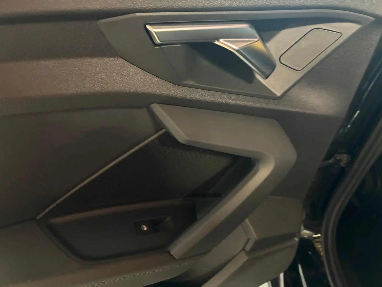 Gros plan sur la porte avant droite noire de l'Audi A3 Sportback 2023 avec accoudoir en similicuir et insert aluminium.
