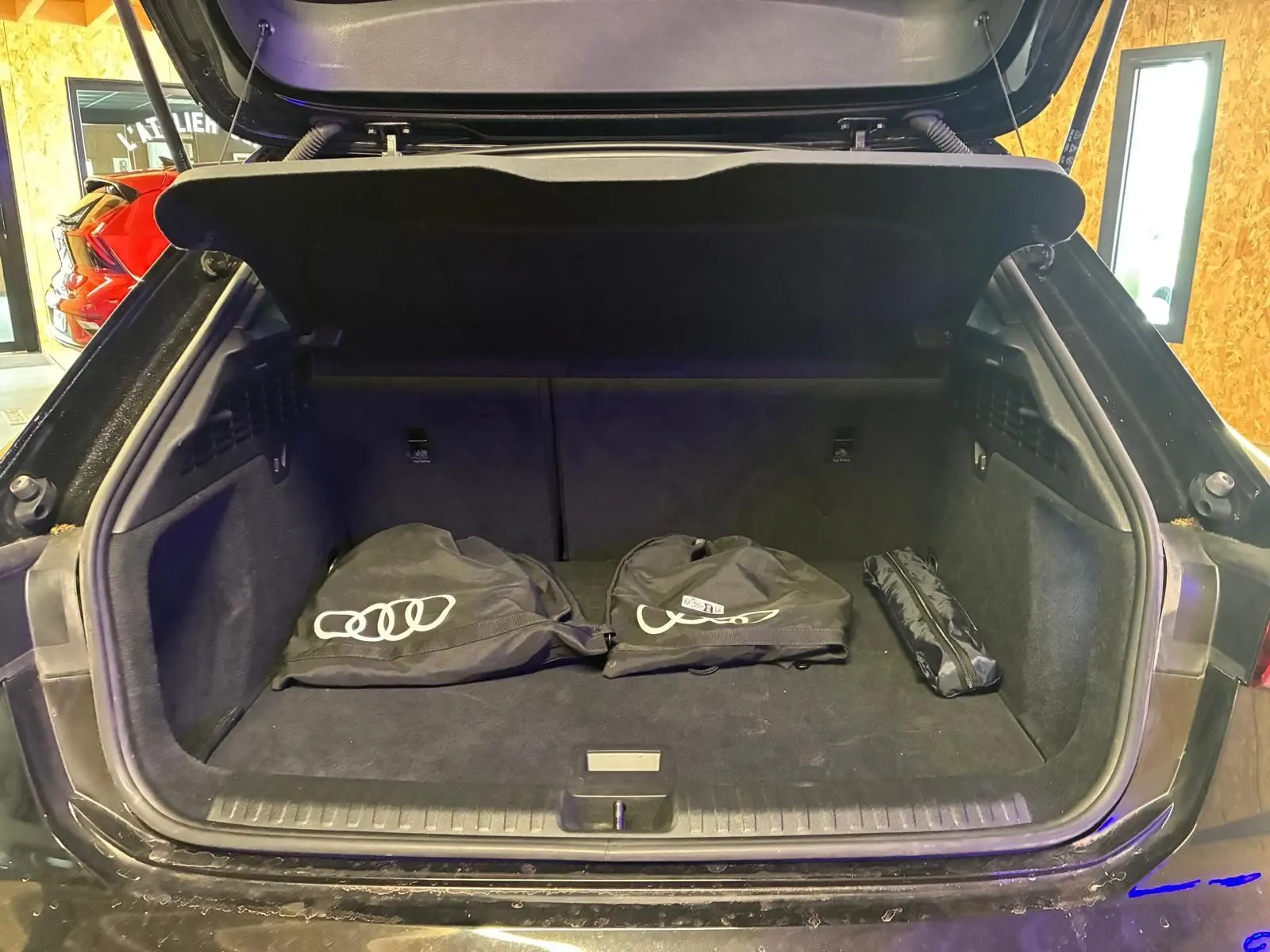 Coffre ouvert d’une Audi A3 Sportback noire, vue arrière, avec housses de protection Audi posées à l’intérieur.