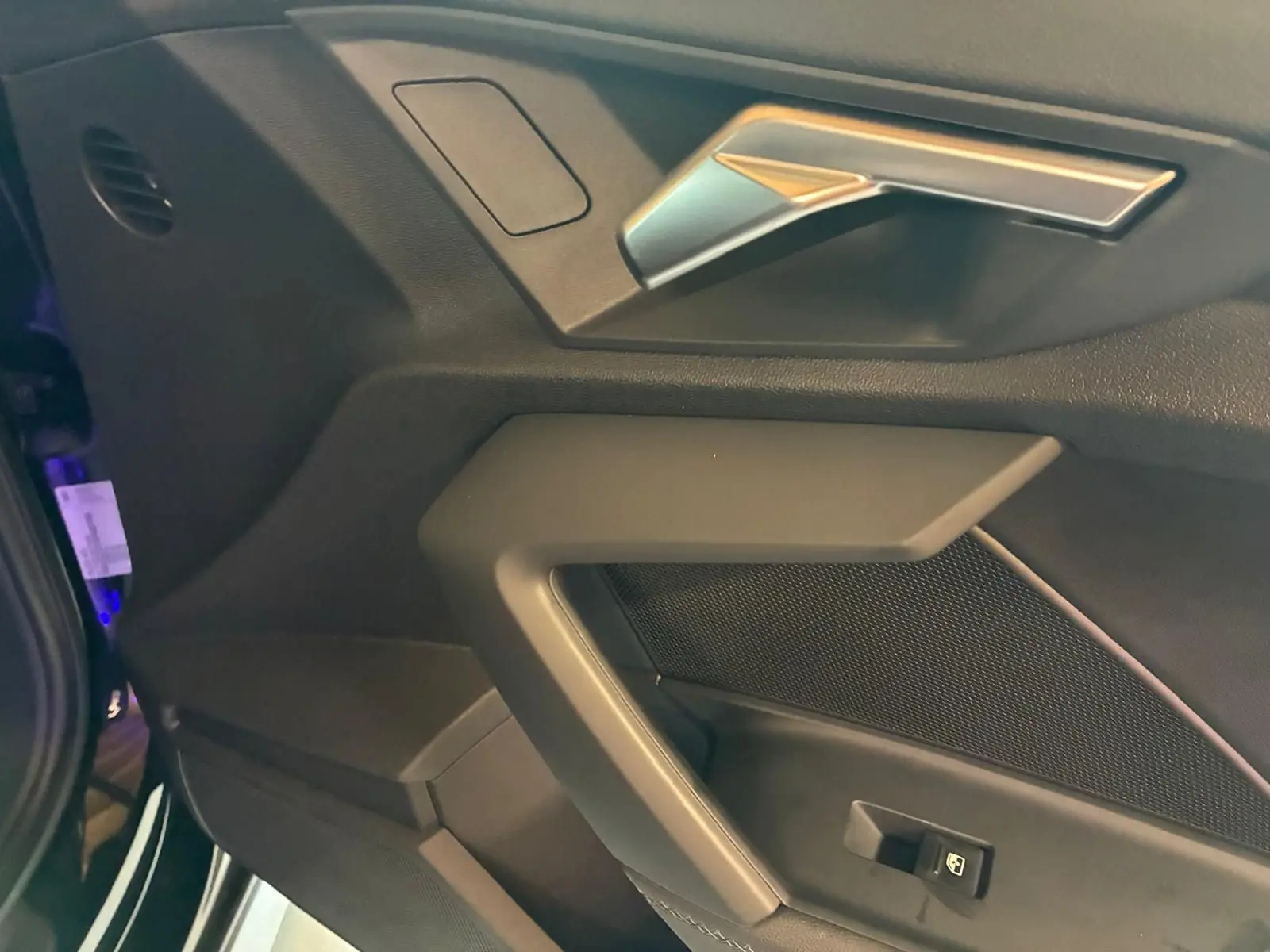 Détail de la portière côté gauche noire de l’Audi A3 Sportback 2023 avec poignée argentée et bouton de lève-vitre.