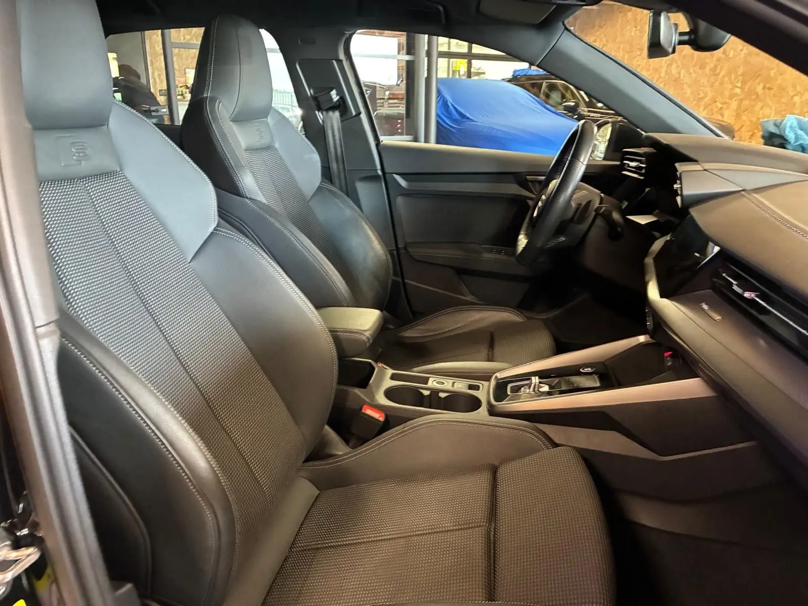 Vue intérieure côté conducteur de l'Audi A3 Sportback 2023, sièges sport noirs avec surpiqûres et volant multifonctions cuir.