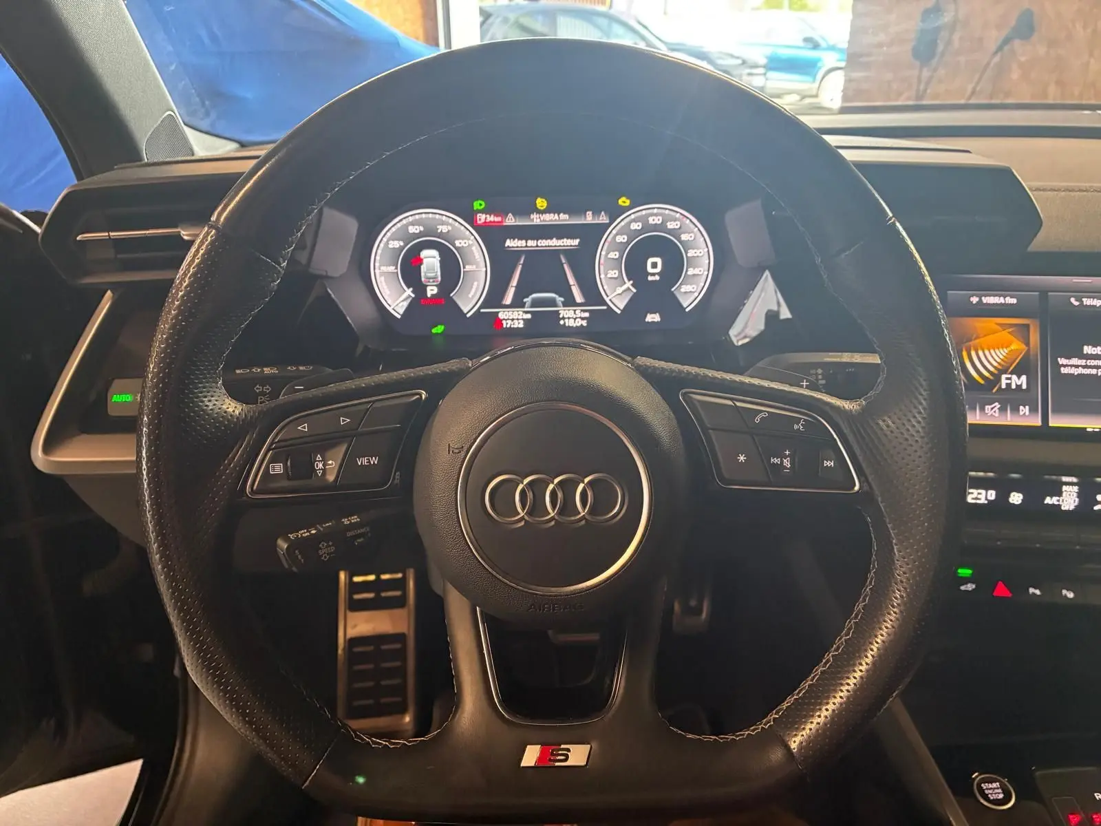 Vue centrée sur le volant cuir perforé S line de l'Audi A3 Sportback 2023 avec tableau de bord numérique allumé.