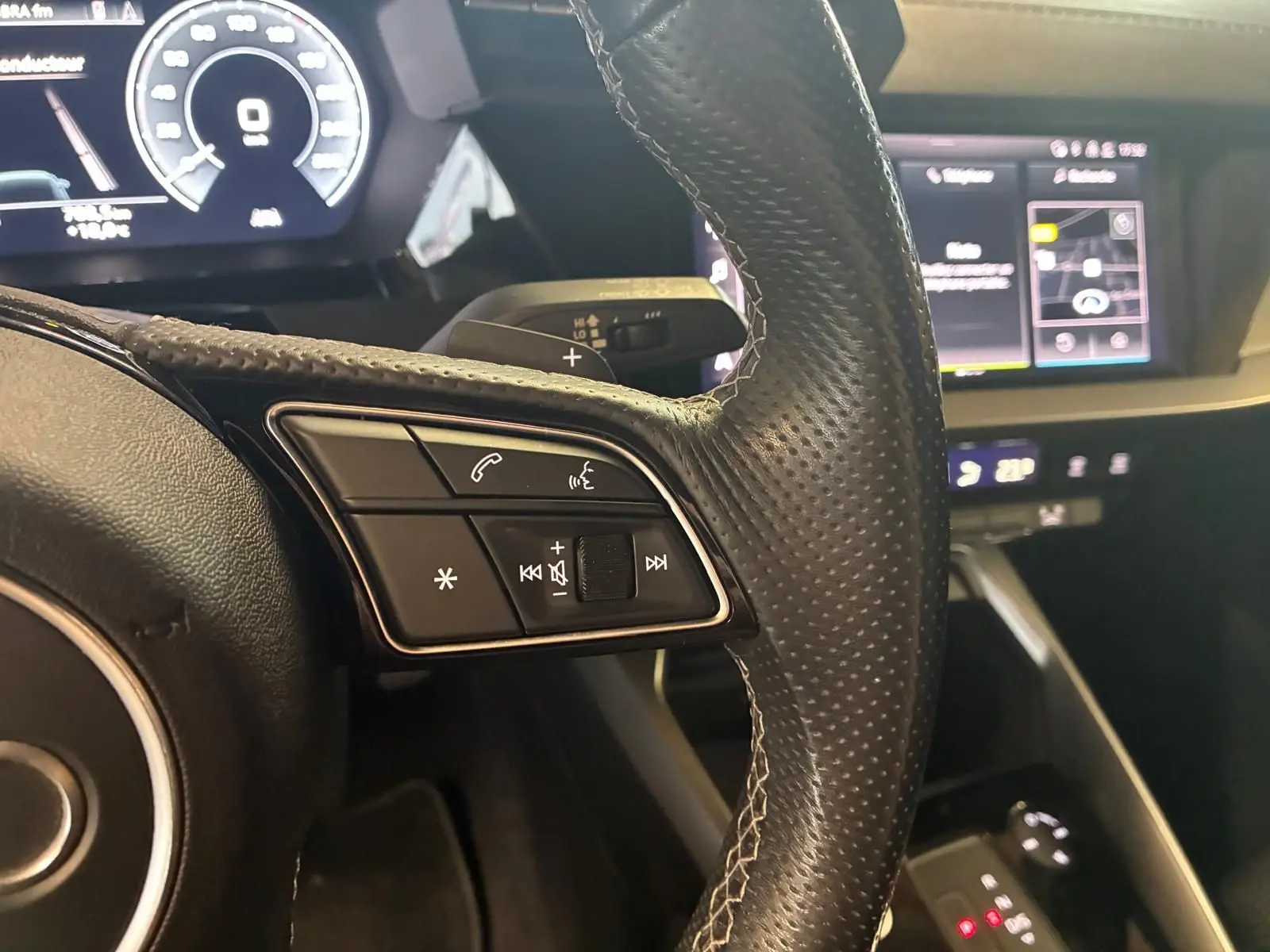 Gros plan sur le volant cuir perforé côté gauche et tableau de bord numérique de l'Audi A3 Sportback noir 2023.