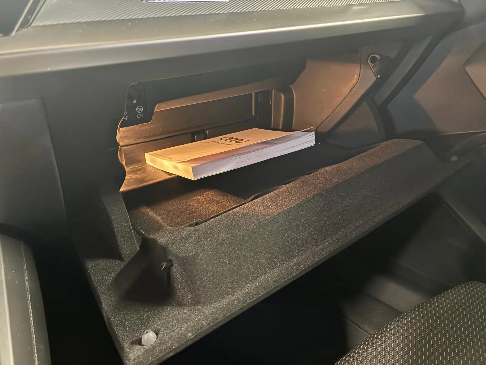 Gant de rangement ouvert côté passager avec manuel Audi posé à l'intérieur d'un Audi A3 Sportback noir 2023.