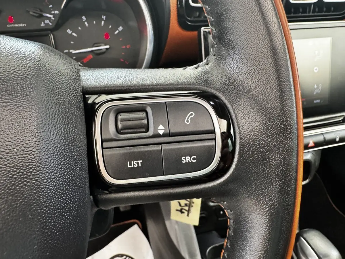 Gros plan sur le volant cuir noir du Citroën C3 Aircross 2020, avec commandes audio et écran tactile en arrière-plan.