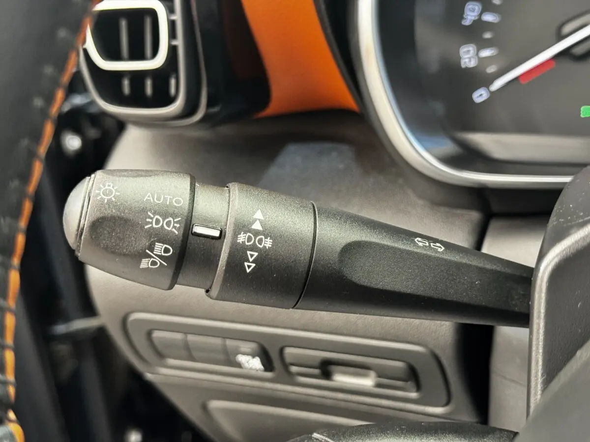 Gros plan sur la manette de commande des feux et clignotants du tableau de bord noir avec surpiqûres orange de la Citroën C3 Aircross.