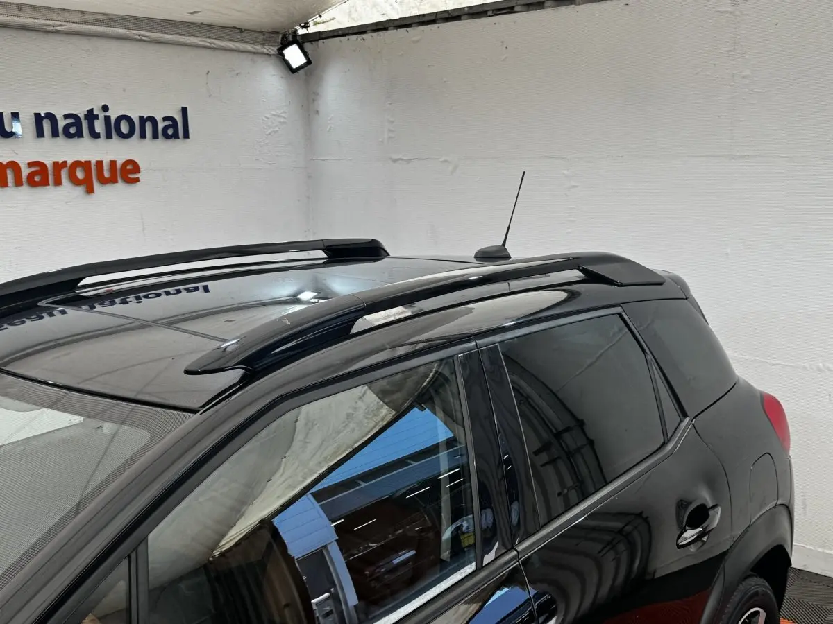 Vue 3/4 arrière gauche d’un Citroën C3 Aircross noir avec barres de toit et vitres teintées dans un garage.