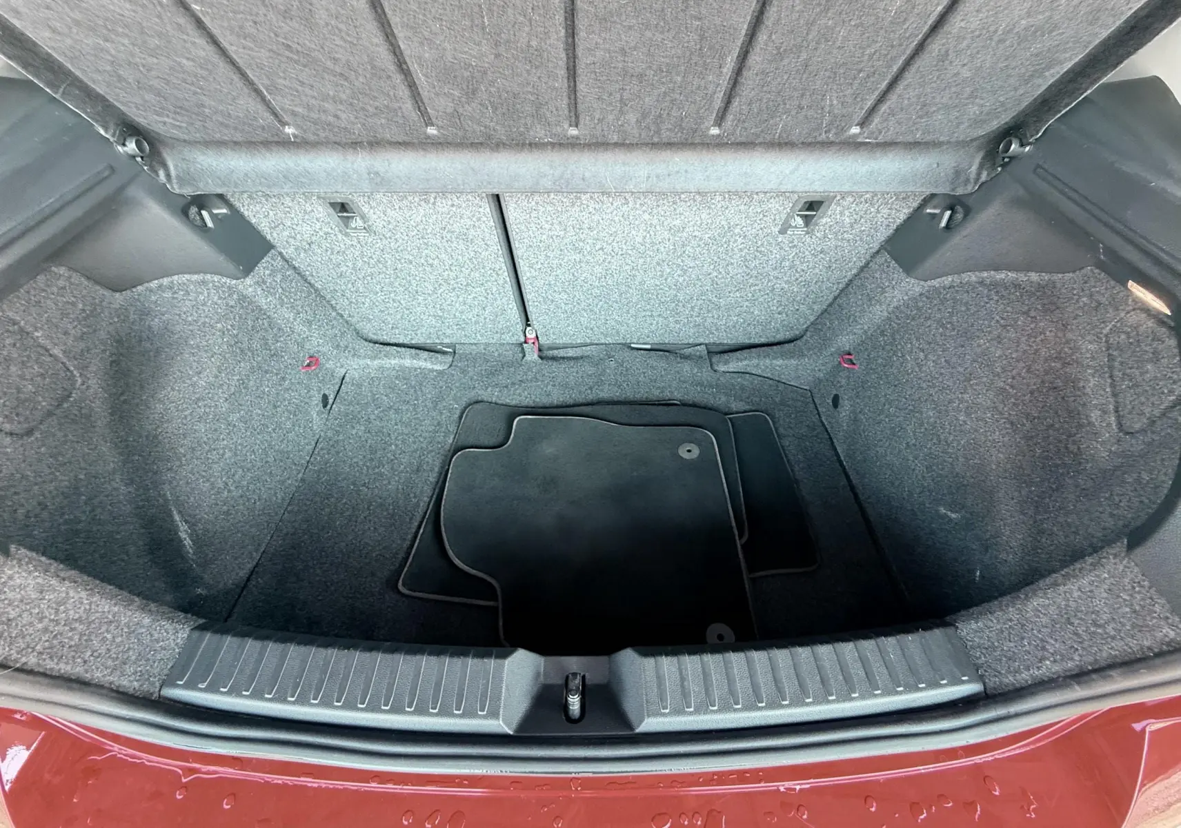 Vue plongeante sur le coffre vide d'une SEAT Ibiza rouge passion métal, avec tapis de sol noir à l'intérieur.