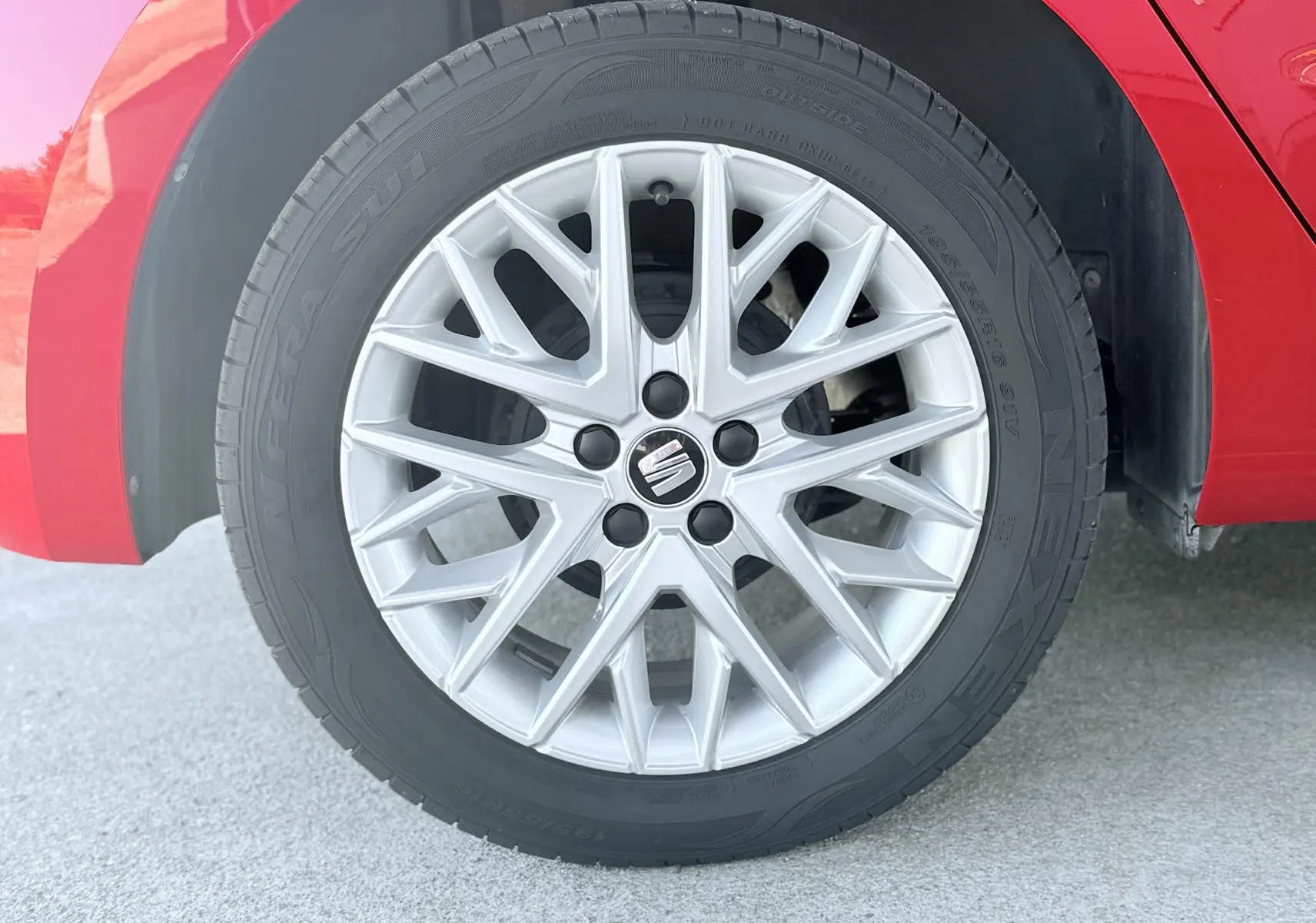 Gros plan sur la roue avant droite d'une SEAT Ibiza rouge passion, avec jante alliage argentée au design fin et moderne.
