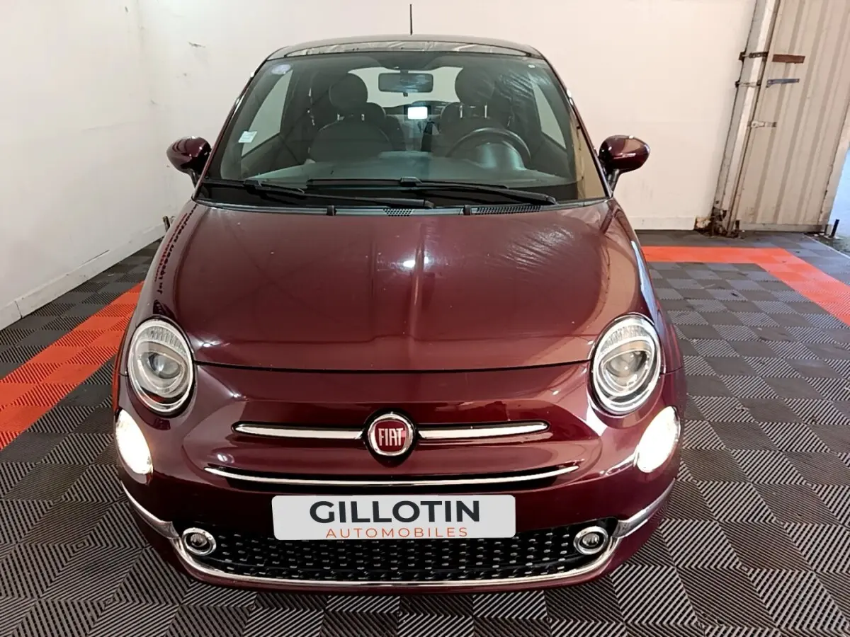 Vue avant d'une FIAT 500 rouge bordeaux avec phares allumés dans un garage intérieur.
