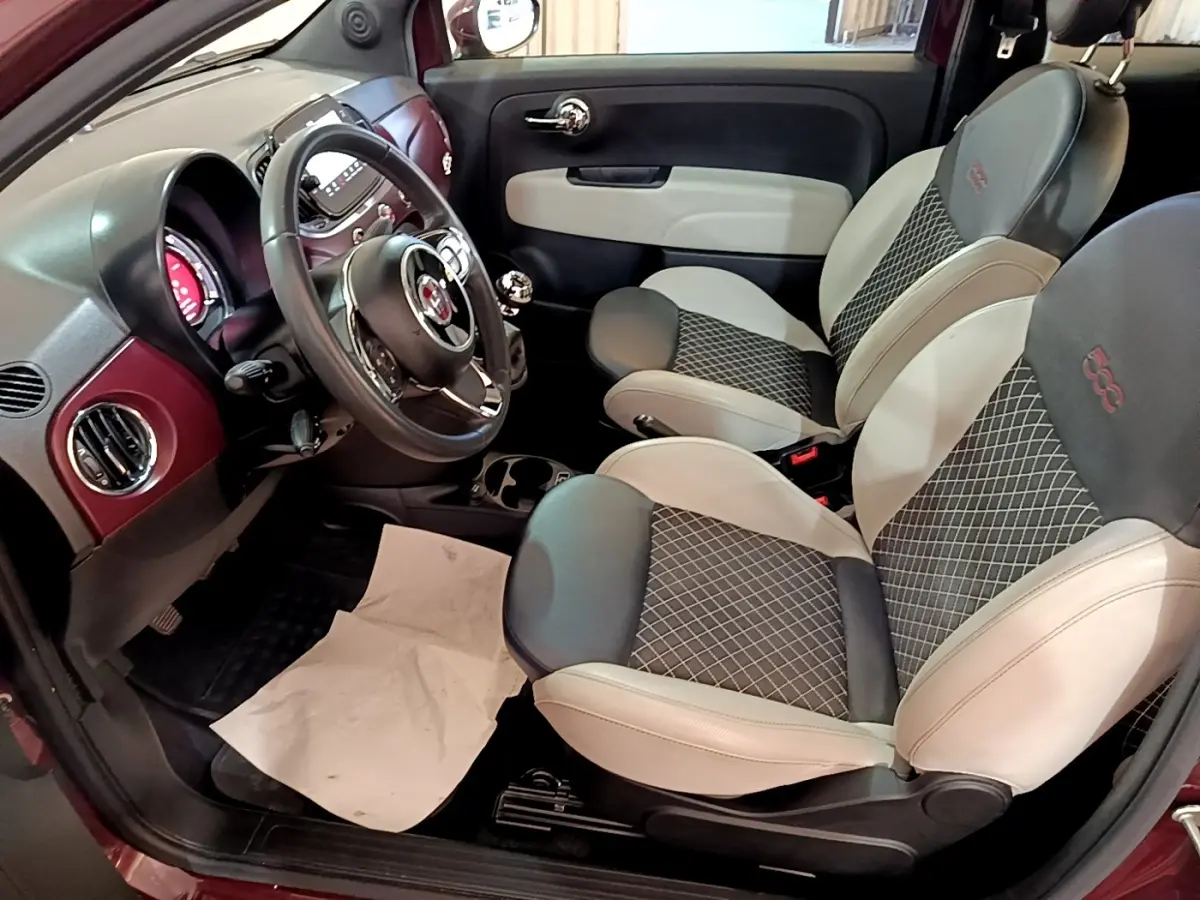 Intérieur côté conducteur de la Fiat 500 rouge 1.0 70ch BSG Star avec sièges bicolores et volant cuir multifonctions.