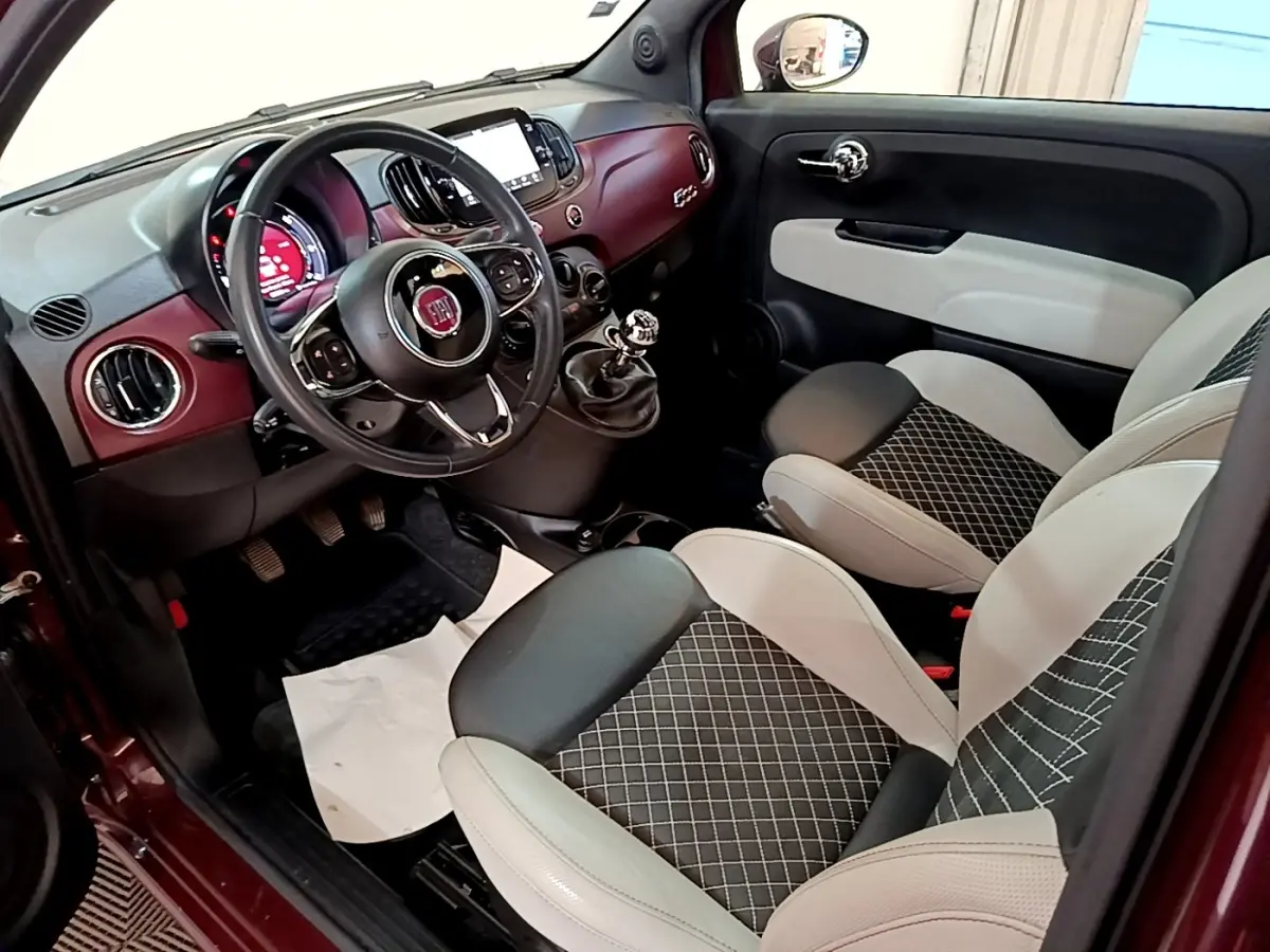 Intérieur côté conducteur de la Fiat 500 rouge, montrant tableau de bord bordeaux et sièges bi-ton noirs et blancs.