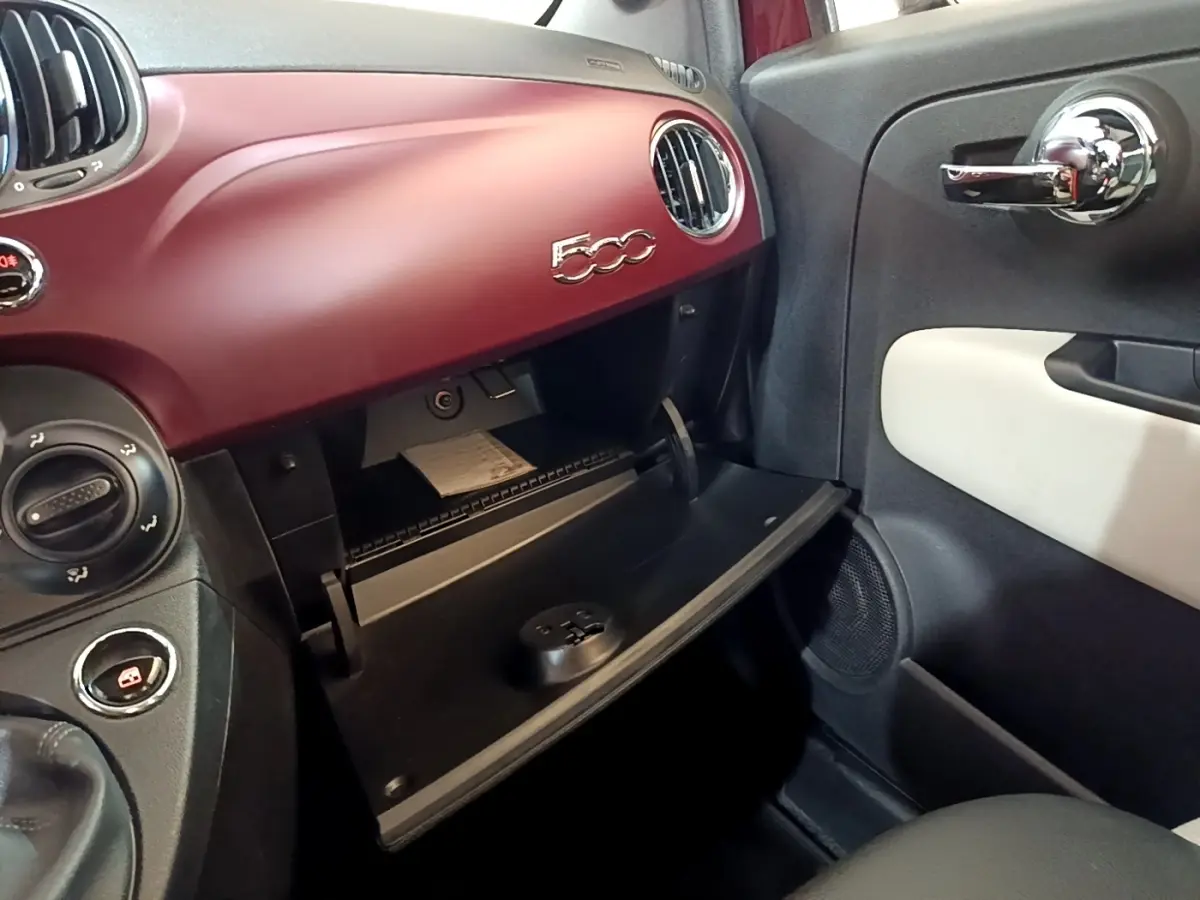 Intérieur côté passager d'une Fiat 500 rouge 2021 avec boîte à gants ouverte et tableau de bord assorti.