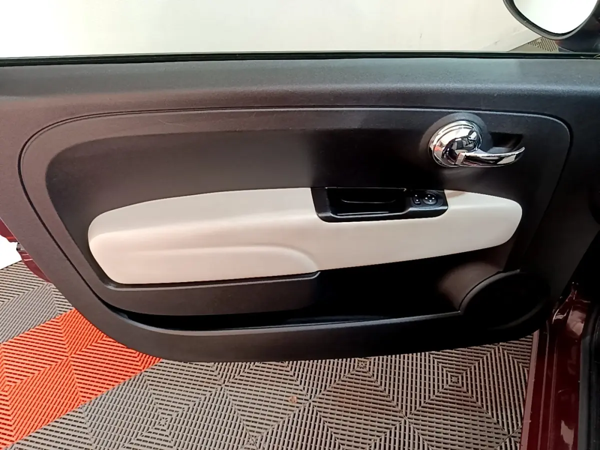 Gros plan sur la porte intérieure côté gauche de la FIAT 500 rouge, avec poignée chromée et garniture beige.