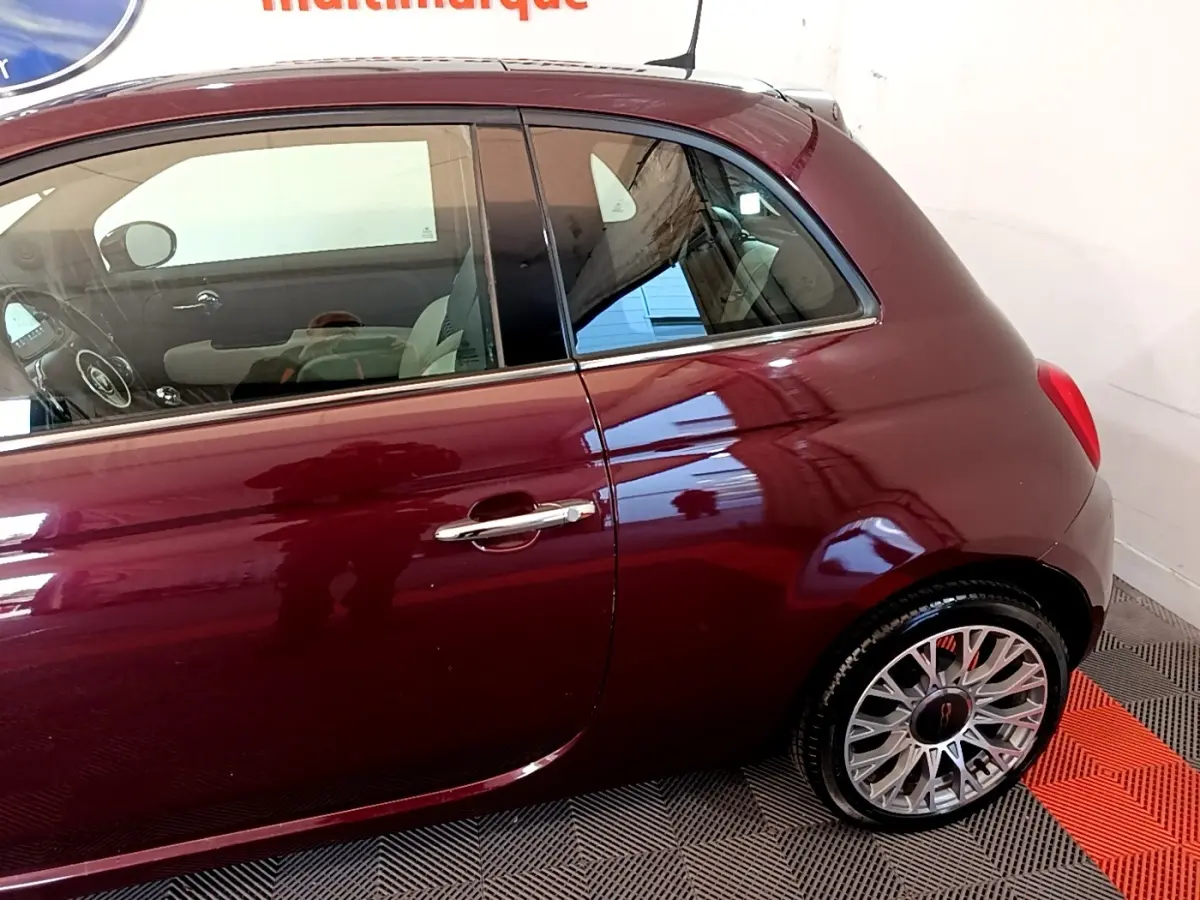 Profil côté gauche d'une FIAT 500 rouge bordeaux 2021 avec jantes alliage et poignée de porte chromée.