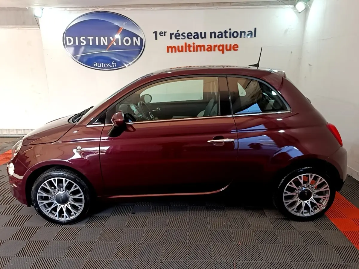 Profil côté gauche d'une FIAT 500 rouge bordeaux 2021, avec jantes alliage et toit compact en intérieur showroom.