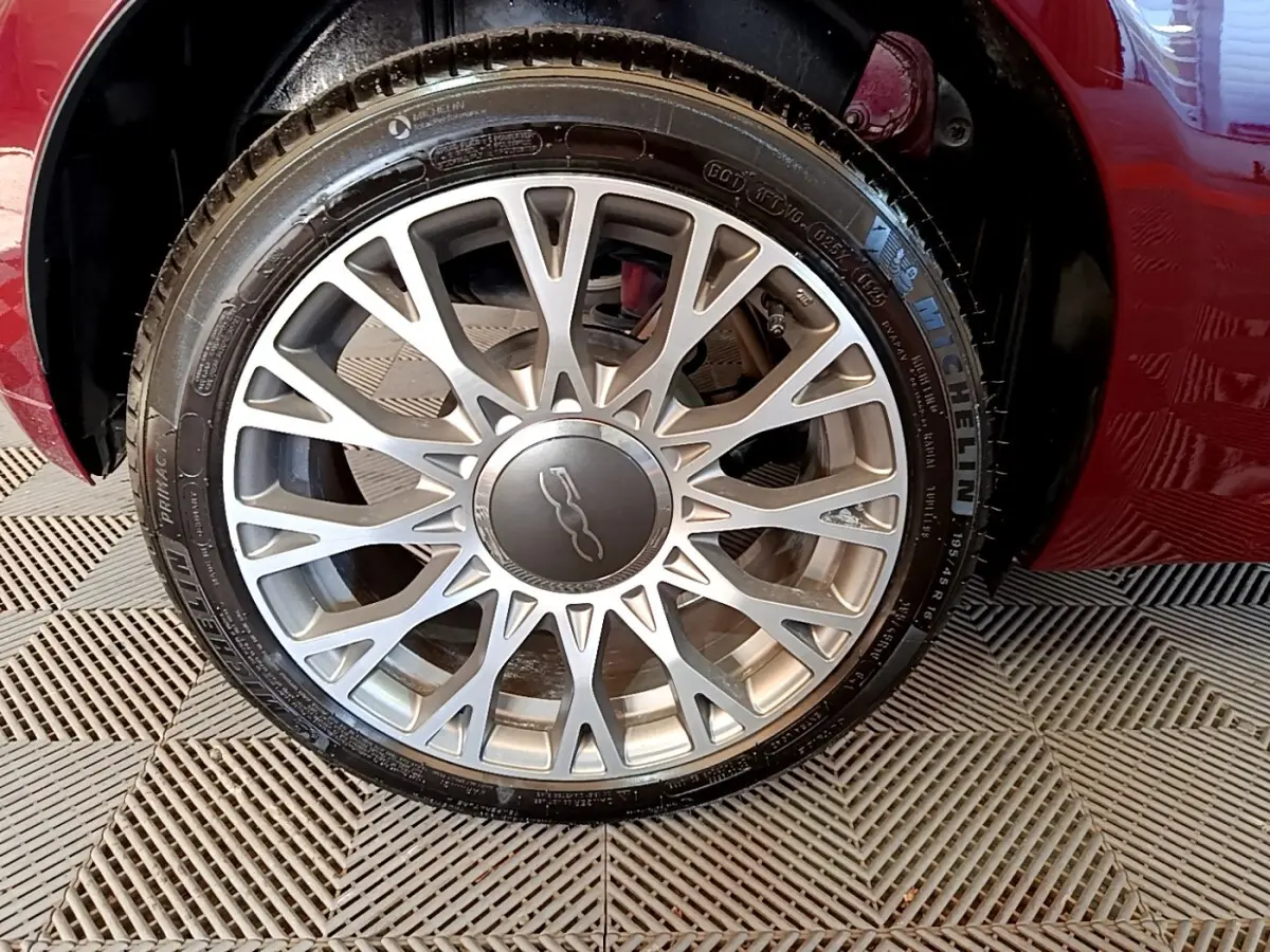 Gros plan sur la roue avant gauche d'une Fiat 500 rouge, mettant en valeur la jante alliage argentée au design étoilé.