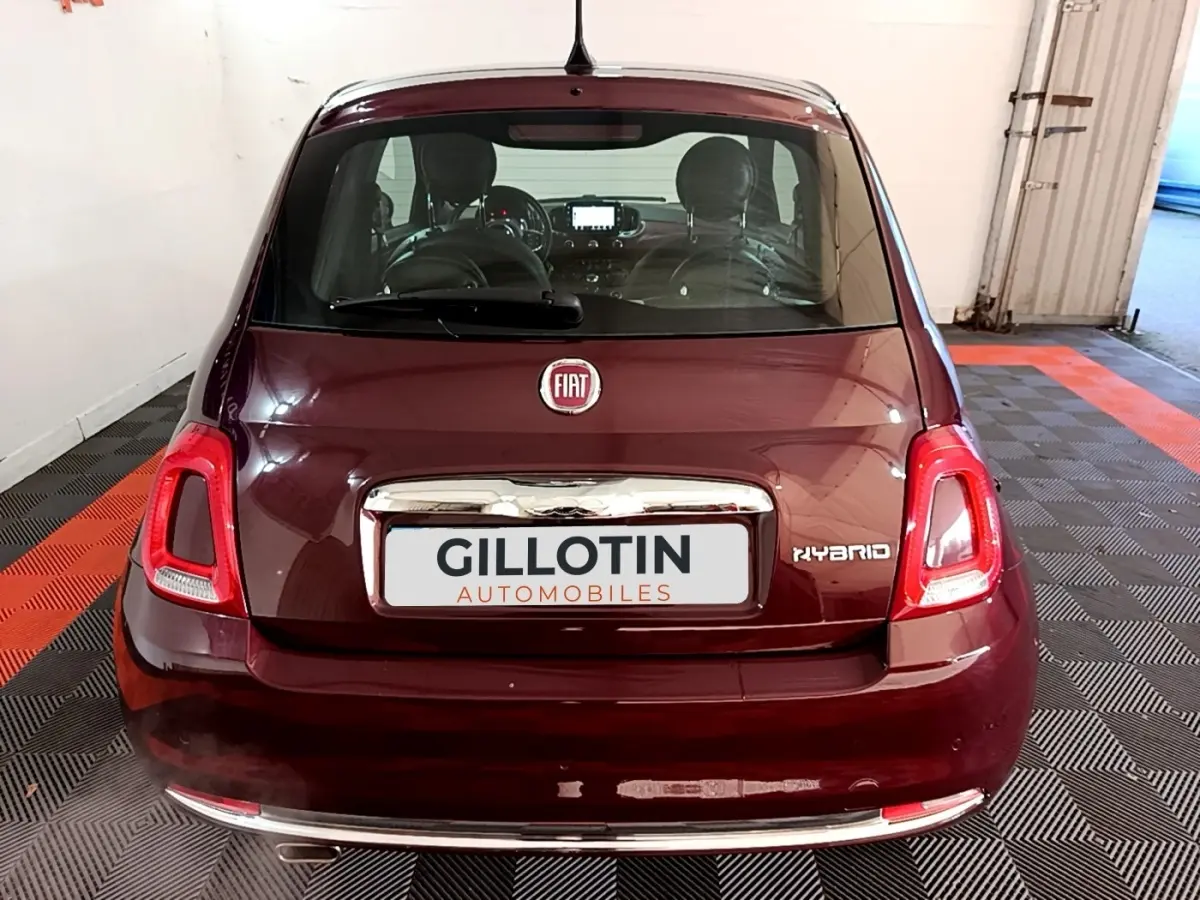 Vue arrière d'une FIAT 500 rouge hybride avec logo FIAT et badge Hybrid visible sur un sol damier noir et rouge.