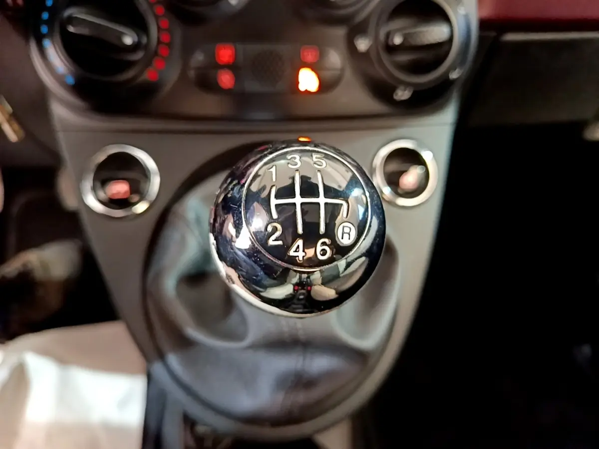 Gros plan sur le levier de vitesses manuel chromé de la FIAT 500 rouge, avec les commandes de climatisation en arrière-plan flou.