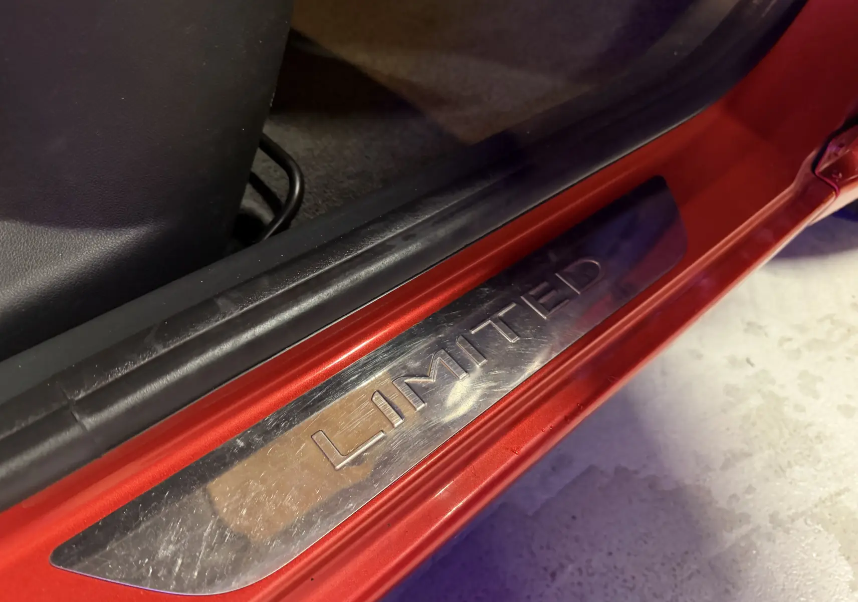 Gros plan sur la plaque de seuil "LIMITED" côté gauche d'une Renault Clio Estate IV rouge de 2015.