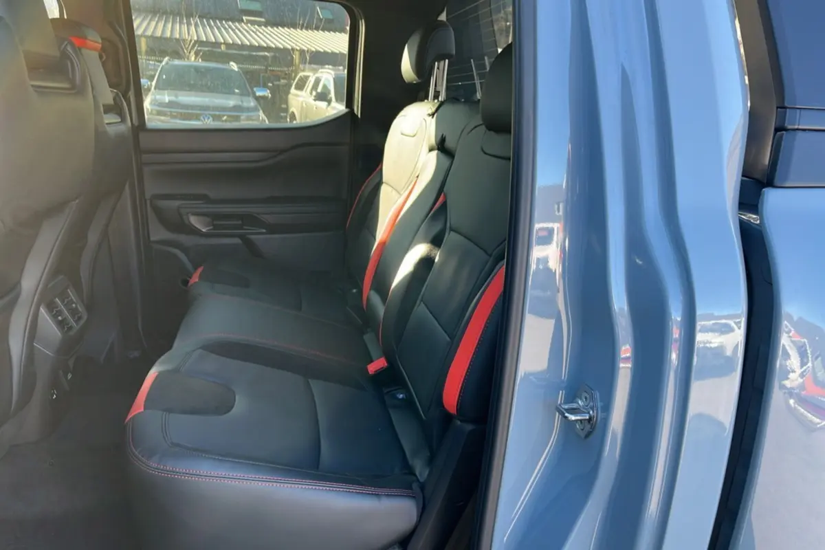 Vue intérieure arrière côté droit du Ford Ranger Raptor 2025, sièges cuir noirs avec surpiqûres rouges, portières gris commandeur.