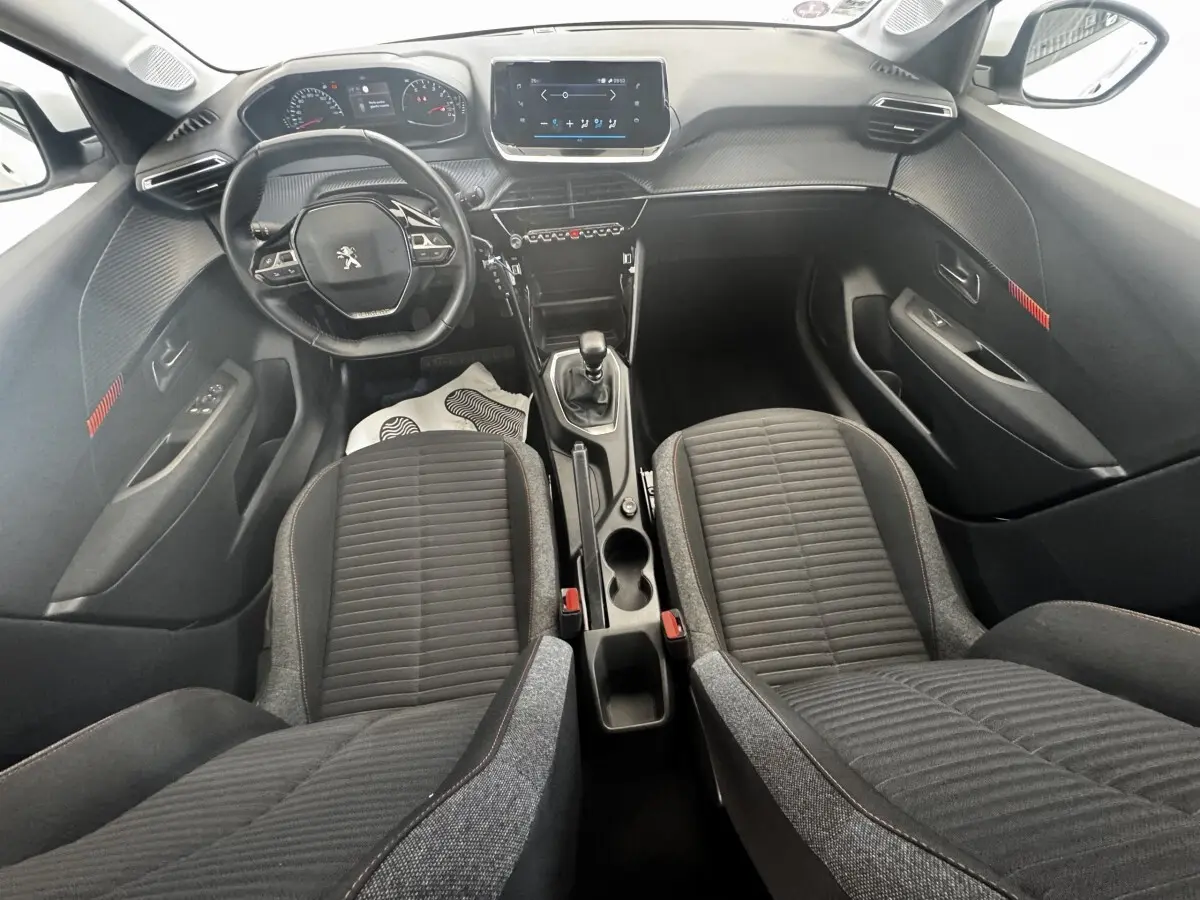 Vue intérieure avant de la Peugeot 208 2020, tableau de bord noir avec écran tactile central et sièges tissu gris.
