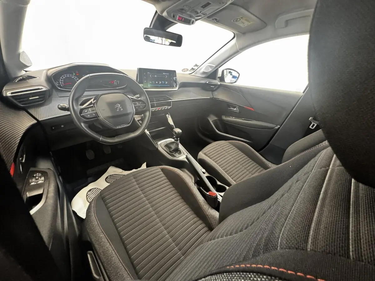 Vue intérieure côté conducteur de la Peugeot 208 blanche, montrant le tableau de bord et la console centrale avec écran tactile.