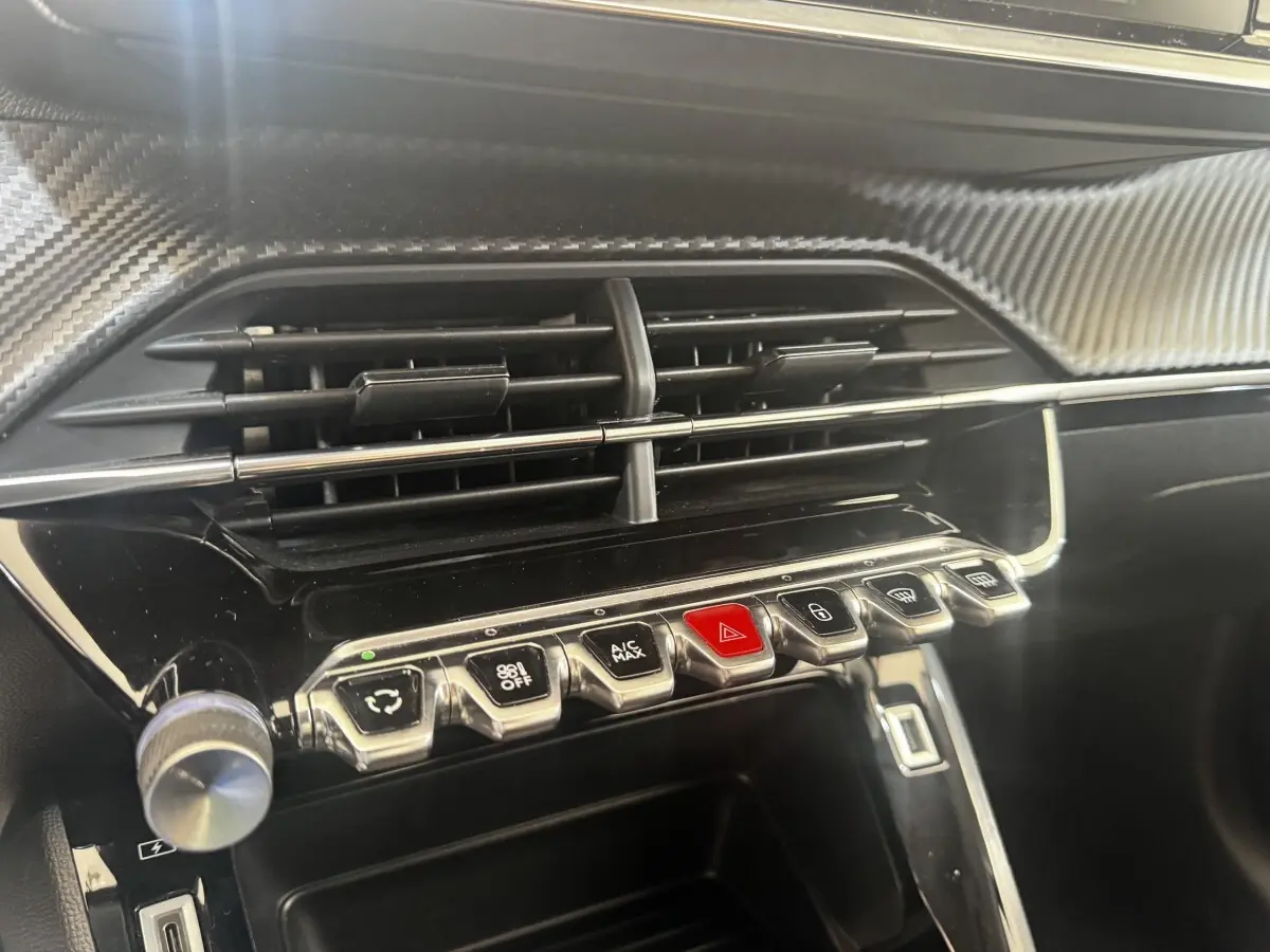 Gros plan sur la console centrale noire brillante de la Peugeot 208 2020 avec boutons chromés et finition carbone.