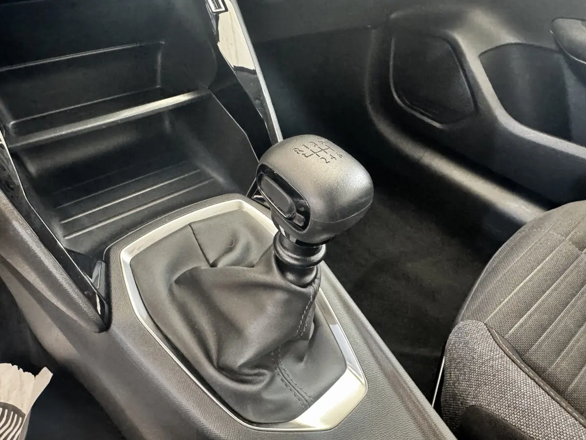 Gros plan sur le levier de vitesses manuel noir de la Peugeot 208 PureTech 100, intérieur avec sellerie grise.