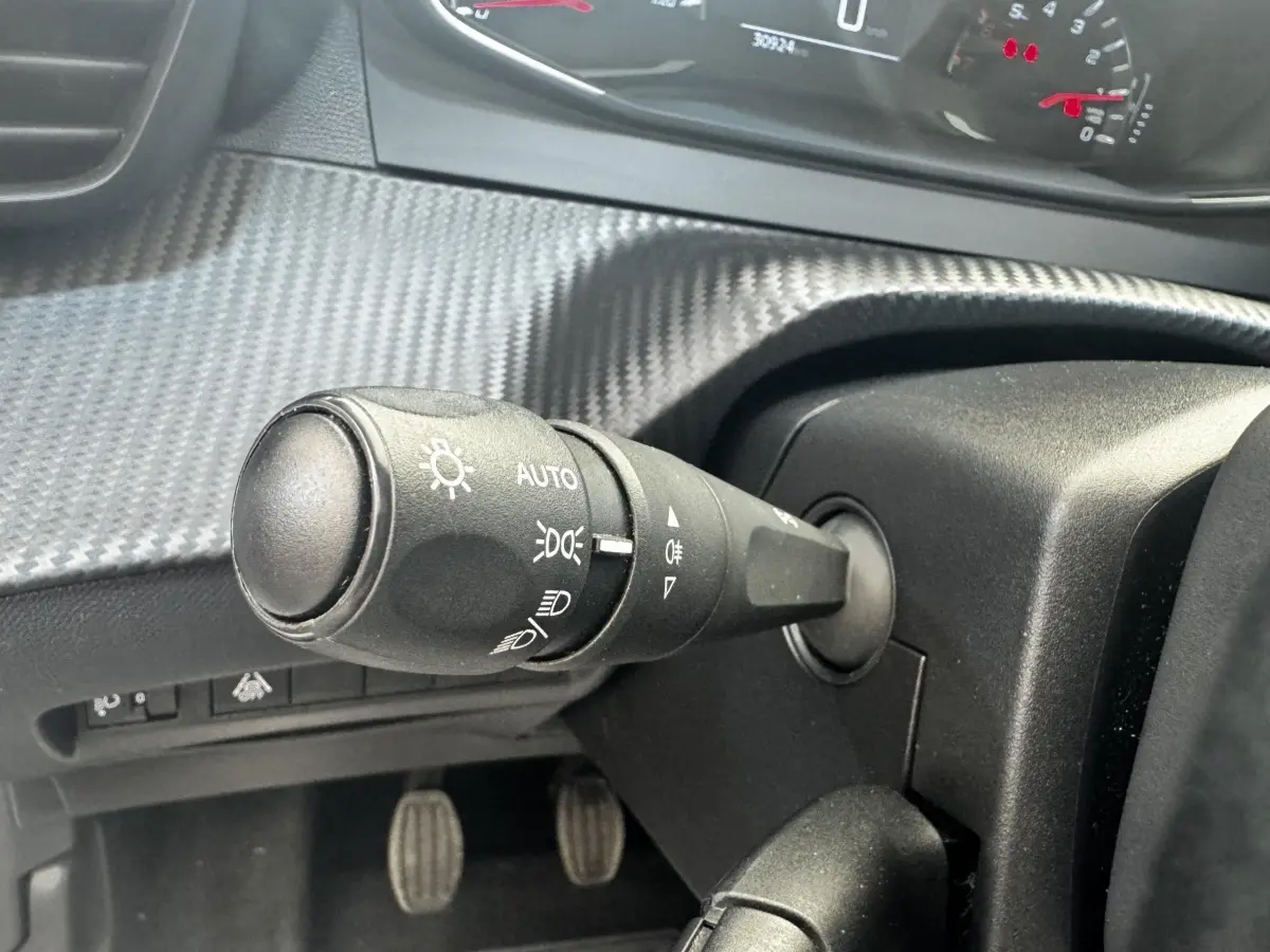 Gros plan sur la commande des phares à gauche du volant dans l’habitacle noir de la Peugeot 208 blanche de 2020.