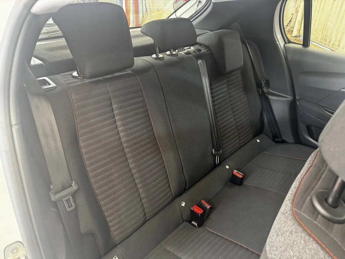 Vue intérieure côté arrière droit montrant la banquette noire avec surpiqûres rouges de la Peugeot 208 blanche 2020.