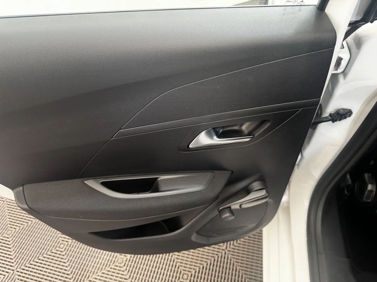 Vue intérieure de la porte arrière droite noire d’une Peugeot 208 blanche, poignée et manivelle de vitre visibles.