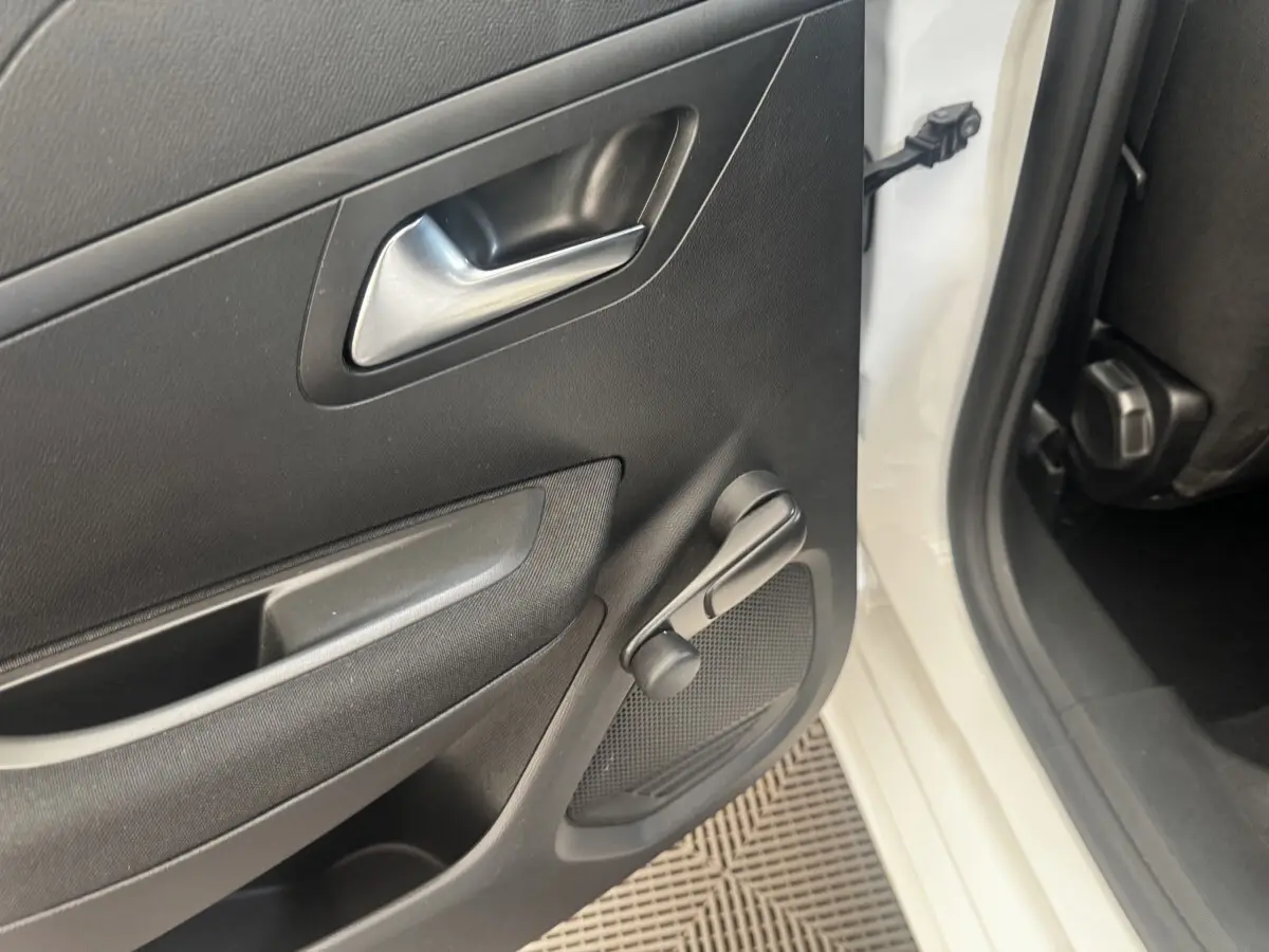 Vue rapprochée de la porte arrière gauche noire d'une Peugeot 208 blanche, avec manivelle de vitre manuelle visible.