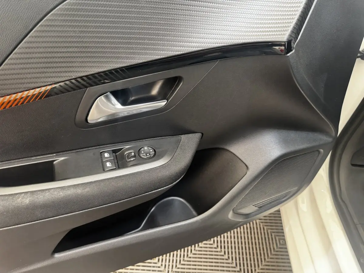 Vue intérieure côté conducteur de la porte noire avec poignée argentée et commandes électriques sur Peugeot 208 blanc.