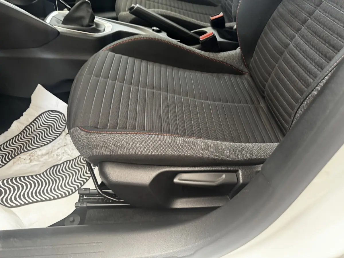 Gros plan sur le siège avant droit noir avec surpiqûres rouges d’une Peugeot 208 blanche, intérieur visible côté conducteur.