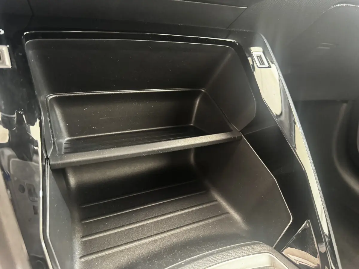 Gros plan sur le rangement intérieur noir du tableau de bord de la Peugeot 208 PureTech 100 blanche.