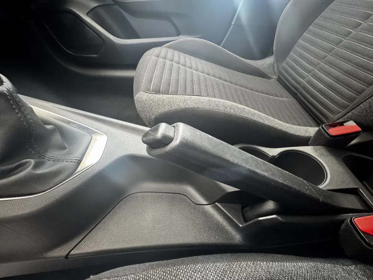 Vue rapprochée de la console centrale avec frein à main levé et siège tissu gris à motifs dans une Peugeot 208 blanche.